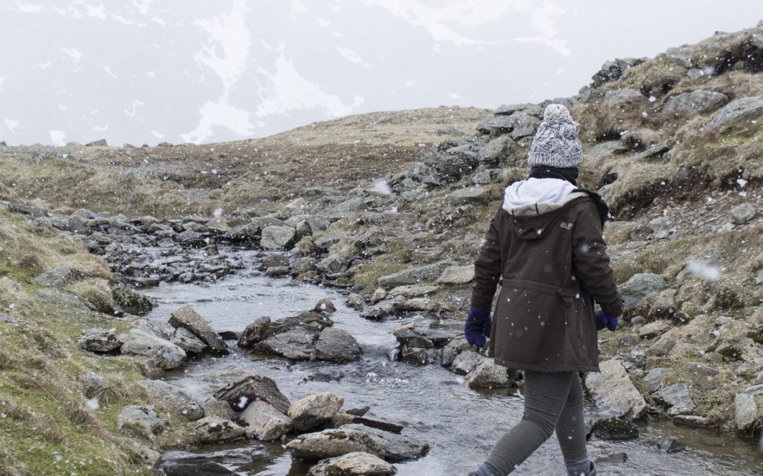 A woman walks alone across a stream bed